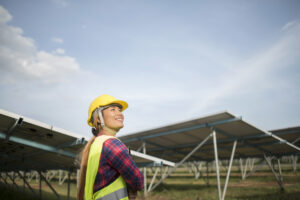 Engenheira sorrindo com capacete de segurança amarelo em usina de energia solar.