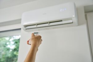 Pessoa usando controle remoto para ajustar o ar-condicionado instalado na parede, com temperatura configurada em 21°C.