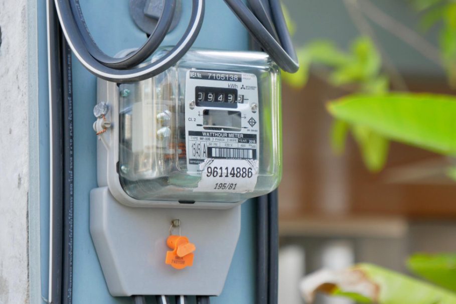 Medidor de energia elétrica instalado em um poste, com fios conectados e vegetação ao fundo.