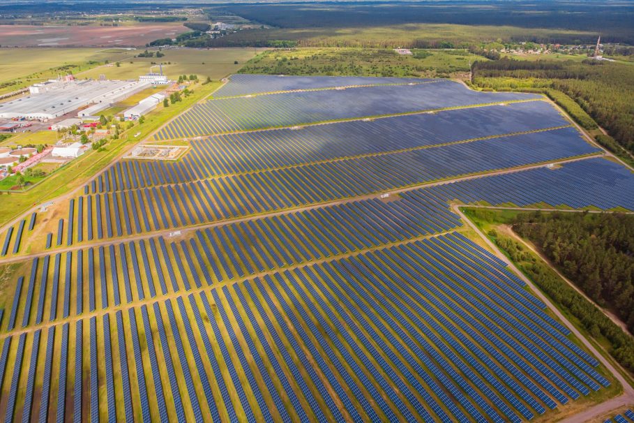 Vista aérea de uma grande usina de energia solar com milhares de painéis solares alinhados em fileiras sobre um campo extenso.